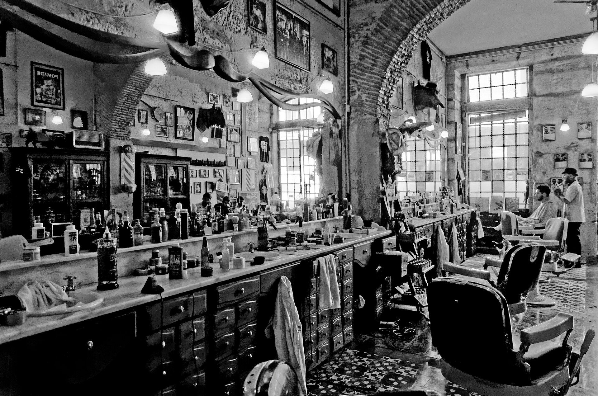 Interior de uma barbearia antiga em Lisboa, com cadeiras de barbeiro, espelhos e frascos nas prateleiras, a preto e branco