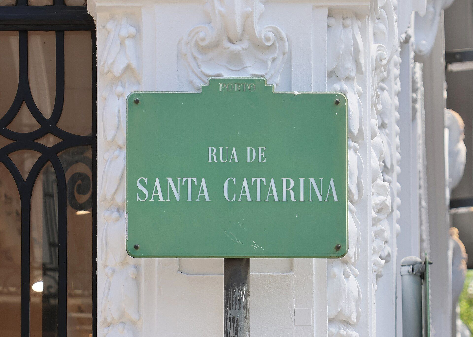 Placa verde da Rua de Santa Catarina, a principal rua de comércio do Porto, numa fachada branca trabalhada